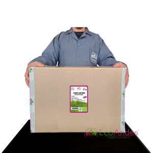 Persona con bata de laboratorio de la marca EcoAndes sosteniendo una caja de 25 kg de Chufa Entera. El empaque muestra una etiqueta con información del producto, certificaciones ecológicas y sello de calidad y envasado artesanal.