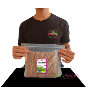 Persona con camiseta de la marca EcoAndes sosteniendo una bolsa transparente con cierre zip de 1kg de Canela en rama. El empaque muestra una etiqueta con información del producto, certificaciones ecológicas y sello de calidad y envasado artesanal.