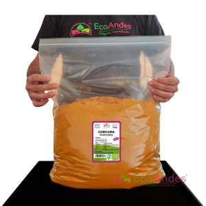 Persona con camiseta de la marca EcoAndes sosteniendo una bolsa transparente con cierre zip de 5 kg de Curcuma en polvo. El empaque muestra una etiqueta con información del producto, certificaciones ecológicas y sello de calidad y envasado artesanal.