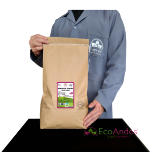 Persona con bata de laboratorio de la marca EcoAndes sosteniendo un saco de papel kraft de 5 kg de Harina de banana. El empaque muestra una etiqueta con información del producto, certificaciones ecológicas y sello de calidad y envasado artesanal.