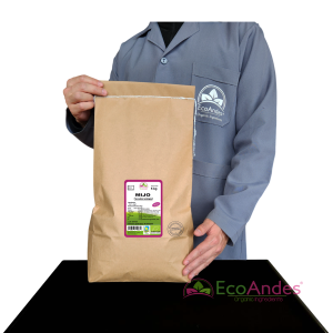 Persona con bata de laboratorio de la marca EcoAndes sosteniendo un saco de papel kraft de 5 kg de mijo en grano orgánico. El empaque muestra una etiqueta con información del producto, certificaciones ecológicas y sello de calidad.